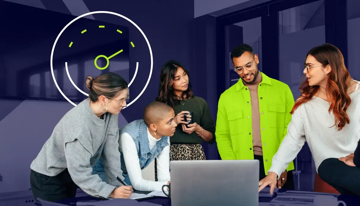 Diverse team collaborating around laptop with speed gauge graphic on office wall behind them