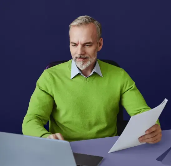 Man in green sweater reviewing documents at desk