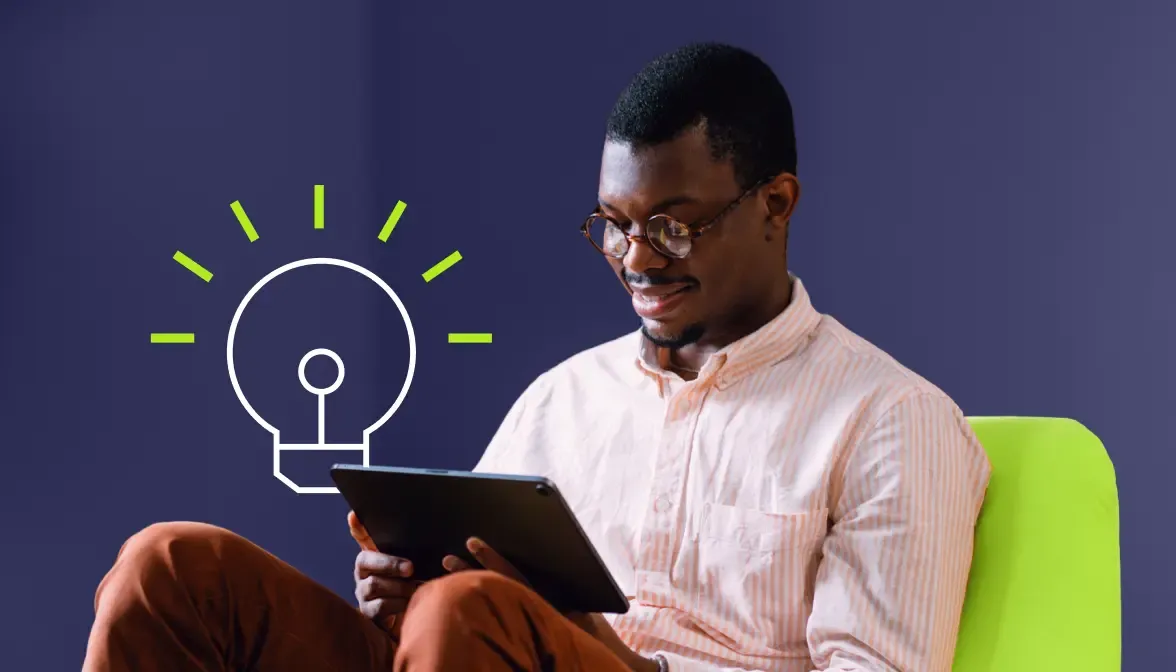 Man with glasses using tablet while seated on green chair with lightbulb icon on wall behind him