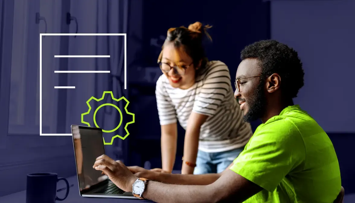 Two coworkers collaborating at laptop with document and gear icon graphic on screen in dark office