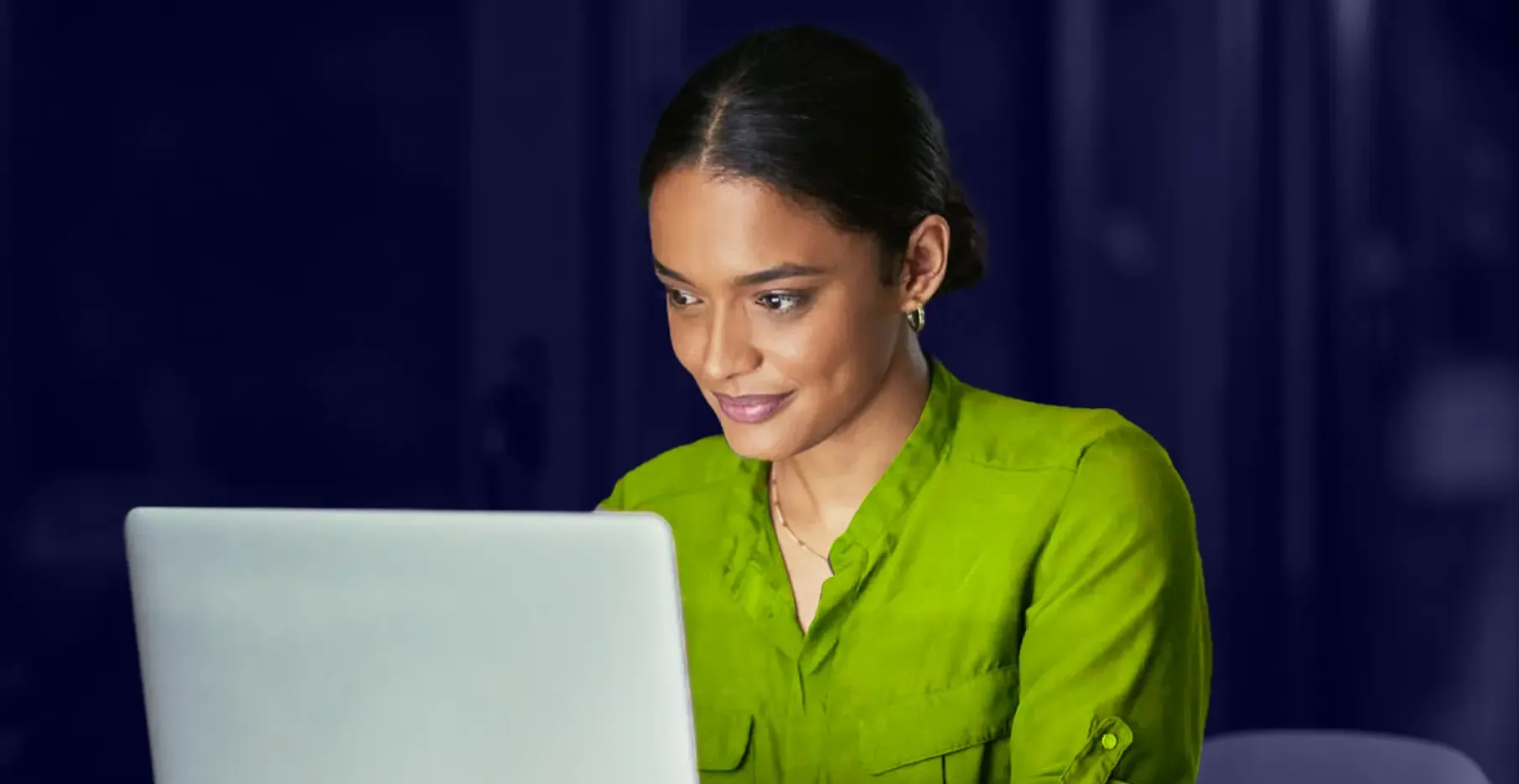 Woman in green blazer smiling while working on laptop